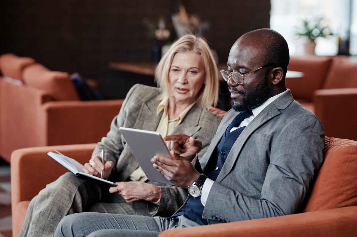 Business owner pointing at a tablet while a colleague takes notes during a planning meeting