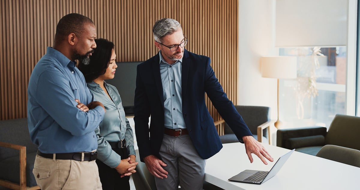 Team of professionals collaborating on a project around a laptop in a modern office